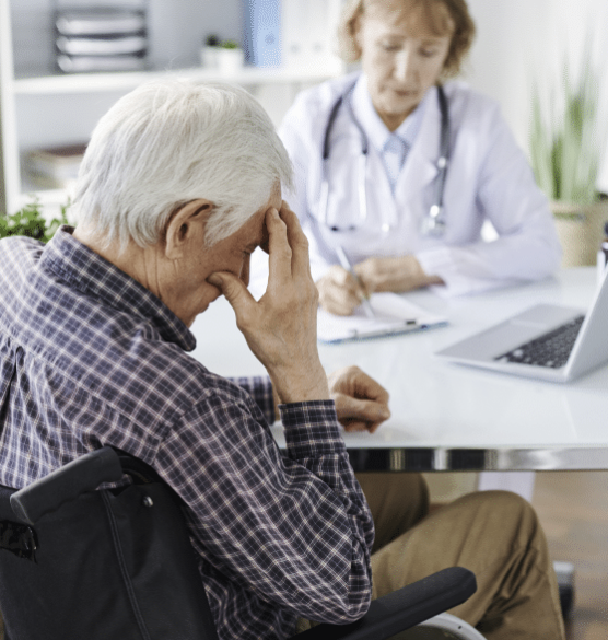 An older man resting his hand against his forehead while a clinician in a white coat takes notes.